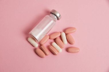 Flatlay, pink pills, white medical capsules and ampoule on pink paper background with copy space