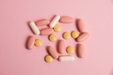 Flat lay, colorful pills and medical capsules on pink background.