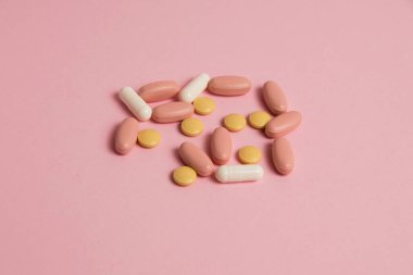 Flat lay, colorful pills and medical capsules on pink background.
