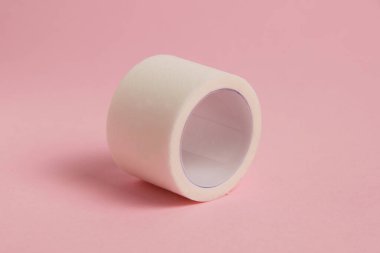 White medical patch on a paper base, for applying bandages, on a pink background.