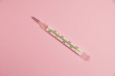 Flatlay, mercury thermometer on paper pink background with copy space.