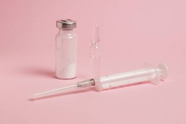 Syringe and two ampoules on pink paper background with copy space.