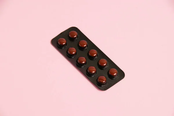 Pills in brown blister on pink paper background with copy space, flat lay