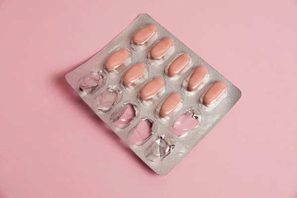 Pink pills in a blister on a pink paper background. Concept of treatment of diseases and support of the body in spring.