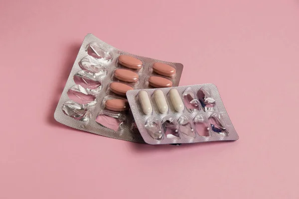 Pills in a blister on a pink paper background. Concept of treatment of diseases and support of the body in spring.