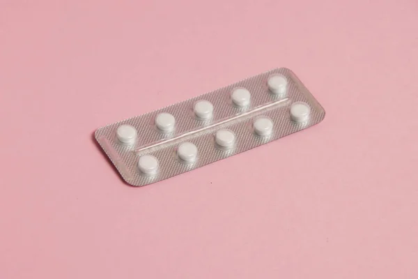 White pills in a blister on a pink paper background. Concept of treatment of diseases and support of the body in spring.