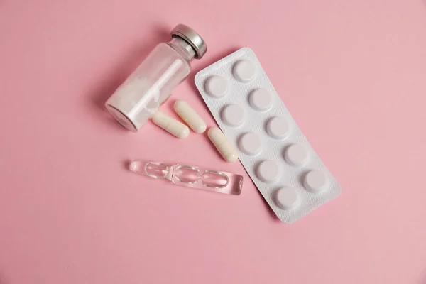 White medical capsules, ampoules with sleeping pill and antibiotic, pills in blister on pink paper background