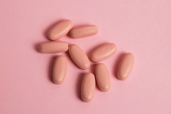 Pink pills on pink paper background with copy space. Concept of taking vitamins in pill form.