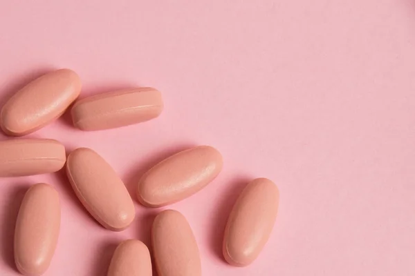 Pink pills on pink paper background with copy space. Concept of taking vitamins in pill form.