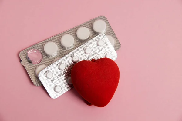 Opened blisters with pills and a red heart on a pink background. Concept of treatment of heart diseases.
