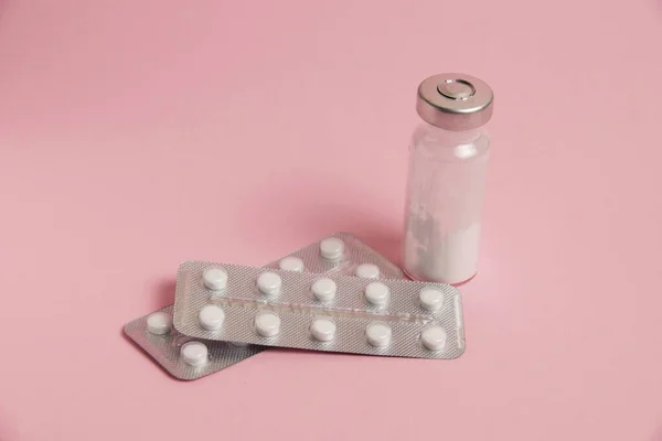 Blisters with pills and ampoule on pink paper background with space for text.