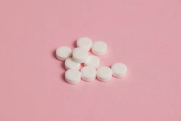 Many white pills on pink paper background with copy space.