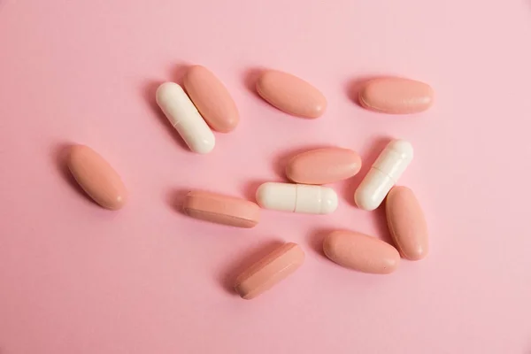 Pink pills and white medical capsules on pink paper background with copy space. The concept of taking vitamins in tablet form.