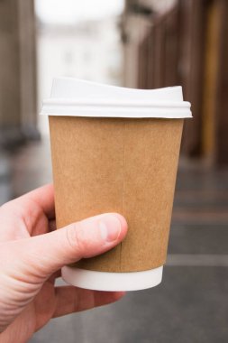 Paper cup with takeaway latte in hand and architecture on background.