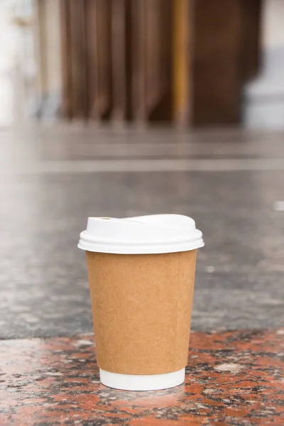 A disposable paper cup of takeaway cocoa on a marble tile.