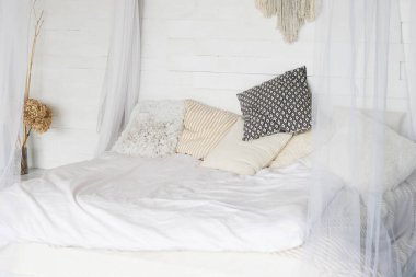 A bright room, a bed with pillows and a white bedspread. Concept of organization of space in the room.