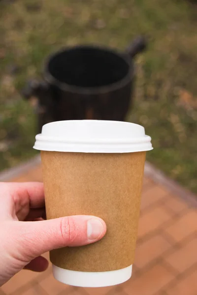 Paper cup in hand on background of urn. The concept of garbage disposal and ecology.