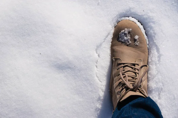 First person view of right foot in womans shoe in snow, background with copy space on left. Snow on beige boots during a winter walk.