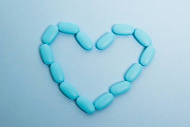 Blue pills laid out on a paper background in the shape of a heart, flatlay. Concept of prevention and treatment of heart diseases.