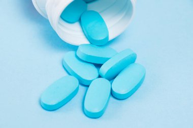 White plastic jar with pills on a blue paper background.