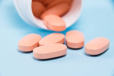 White plastic jar with pink pills of vitamins for women on a blue background.