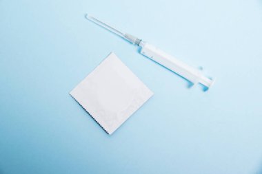 A condom in a package and a syringe on a soft blue background. Concept of protection against sexually transmitted diseases