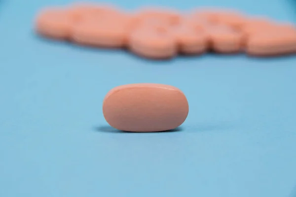 Pink pill macro on a blue paper background and many pills in the background.