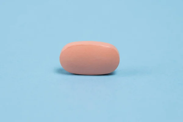 Pink pill macro on blue paper background with copy space.