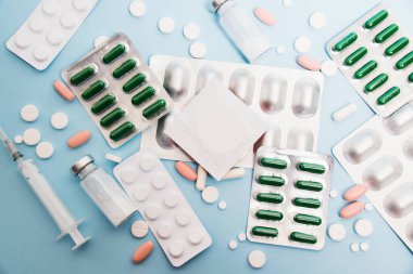 Medical background, flatlay, condom, ampoules, syringe and pills on soft blue paper background. The concept of treatment and protection against venereal diseases