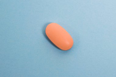 Pink pill macro on blue paper background with copy space.