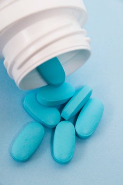 White plastic jar with pills on blue paper background vertical format.