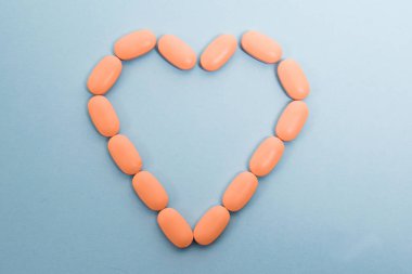 Pink pills laid out on a paper background in the shape of a heart, flatlay. Concept of prevention and treatment of heart diseases.
