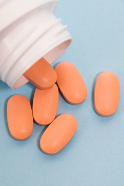 White plastic jar with pink pills of vitamins for women on a blue background.
