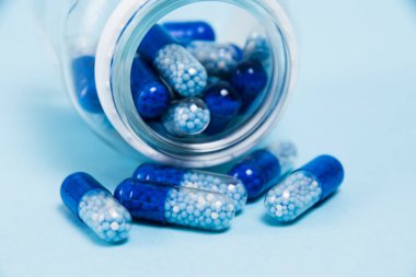 A transparent glass jar with vitamins in tablet form on a blue paper background.