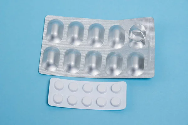 Blisters with pills on a blue paper background, antibiotics and probiotics. Concept of correct treatment.