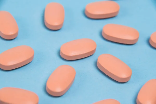 Pattern, pink capsules with vitamins on a blue paper background, flatlay.