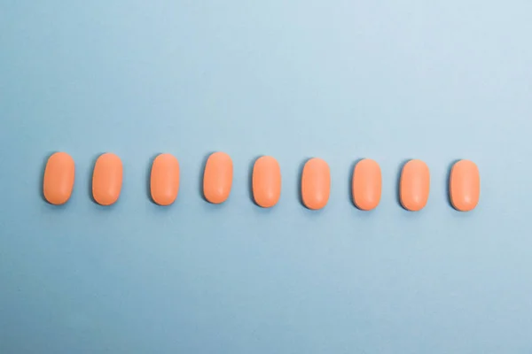 Pattern, pink capsules with vitamins on a blue paper background, flatlay.
