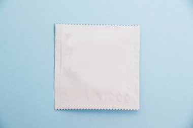 Condom in white packaging on a soft blue background.