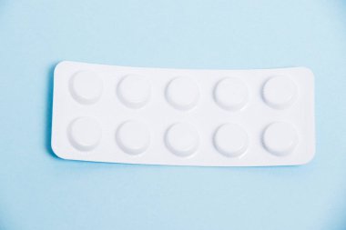 White blister pack with antibiotic pills on blue paper background, top view.