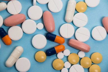 Flatlay, many colorful pills on blue paper background.
