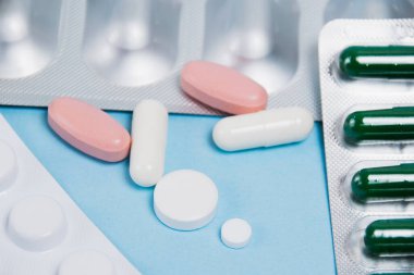 Many multi-colored pills macro in blisters and without on soft blue paper background.