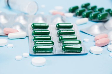 Many multi-colored pills macro in blisters and without on soft blue paper background.