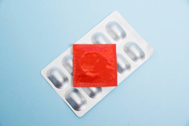 Medical background with copy space, flat lay, condom in red package and pills in gray blister. Concept of contraception and protection from unwanted pregnancy