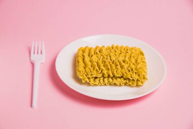 Beyaz tabakta, pembe arka planda plastik çatalla hazır şehriye. Modern dünyada fast food.