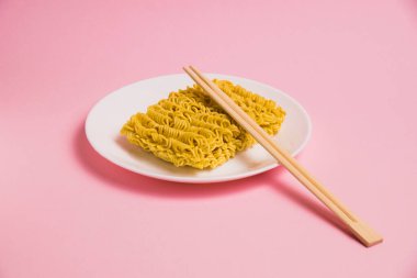 Beyaz tabakta hazır şehriye ve pembe arka planda çubuklar..