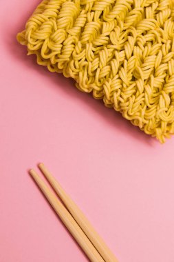 Yemek çubukları ve pembe arka planda çiğ erişte, düz uzanmış..