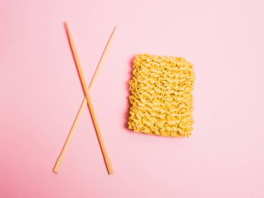 Düz döşeme, yemek çubukları ve pembe kağıtta çiğ erişte.