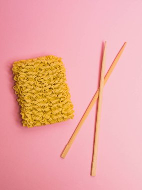 Düz döşeme, yemek çubukları ve pembe kağıtta çiğ erişte.
