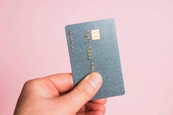 Bank card with a chip macro, in a human hand, on a pink background. Modern technologies of payment for goods in the store and online.