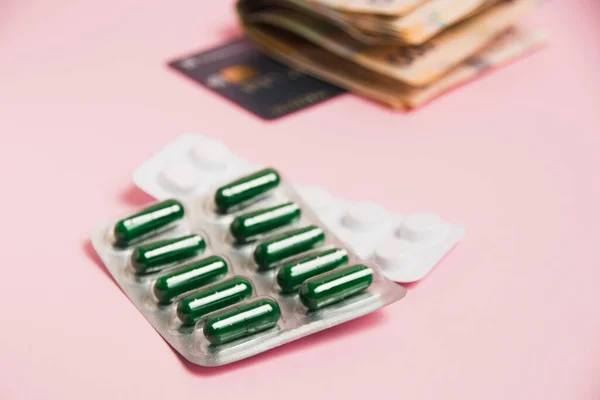 Pills, money and a bank card on a pink background. Concept of ordering medicine online.